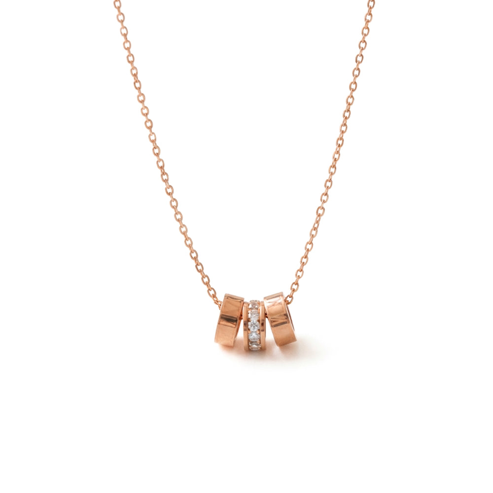 Rose gold necklace with a pendant made of three interlocking cylindrical rings, with the center ring set with clear gemstones, on a white background.