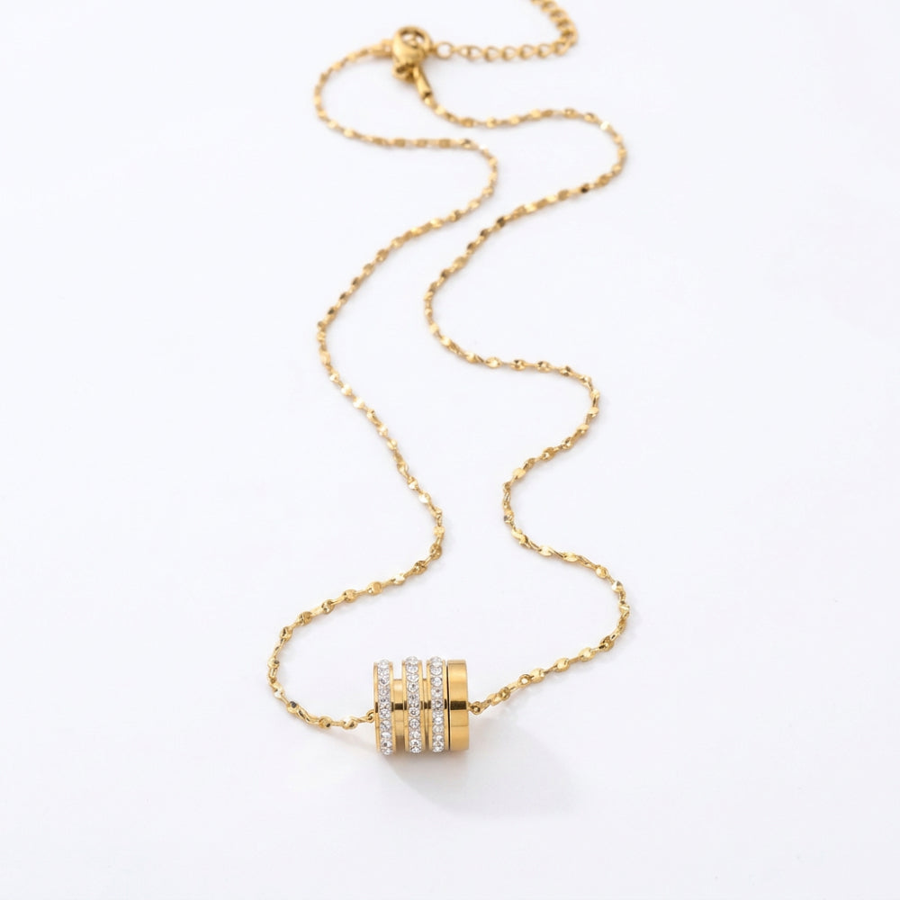 A gold chain necklace with a cylindrical pendant featuring three horizontal rows of small clear stones, displayed on a clean white background.
