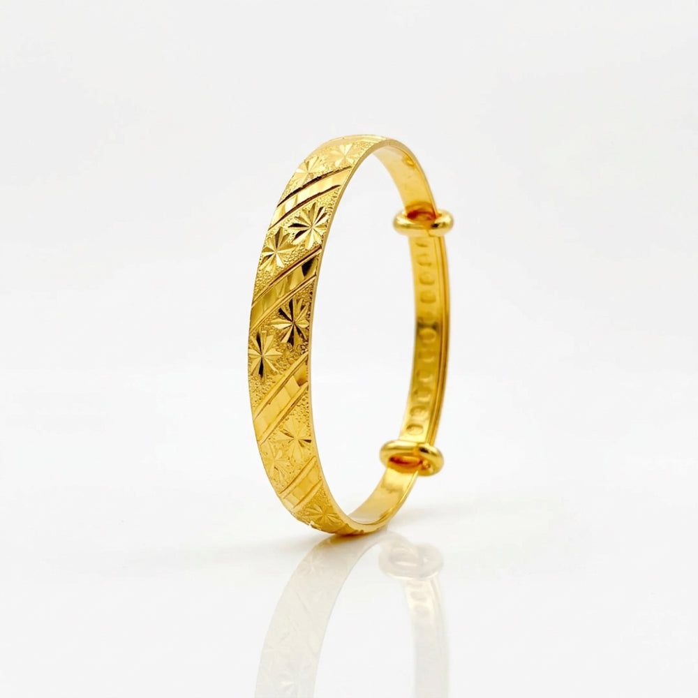 A gold-plated bangle bracelet with intricate starburst and diagonal line engravings, standing upright on a reflective white surface.