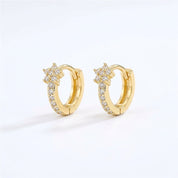 A pair of gold huggie hoop earrings with a star-shaped cluster of clear pavé stones on the front, set against a clean white background.