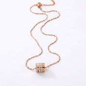 A rose gold chain necklace with a cylindrical pendant featuring three horizontal rows of small clear stones, displayed on a clean white background.