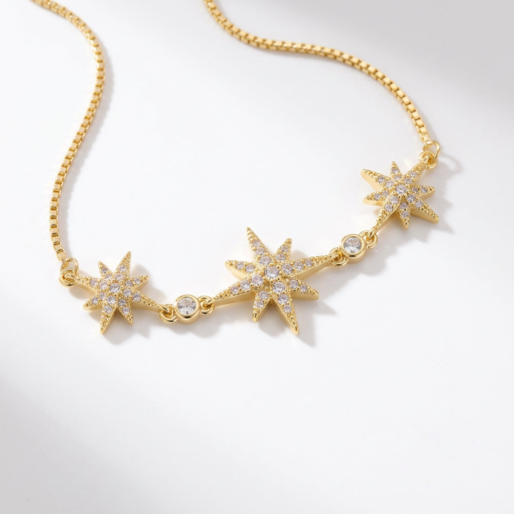 A gold chain necklace featuring three starburst charms paved with clear stones, displayed on a clean white background.