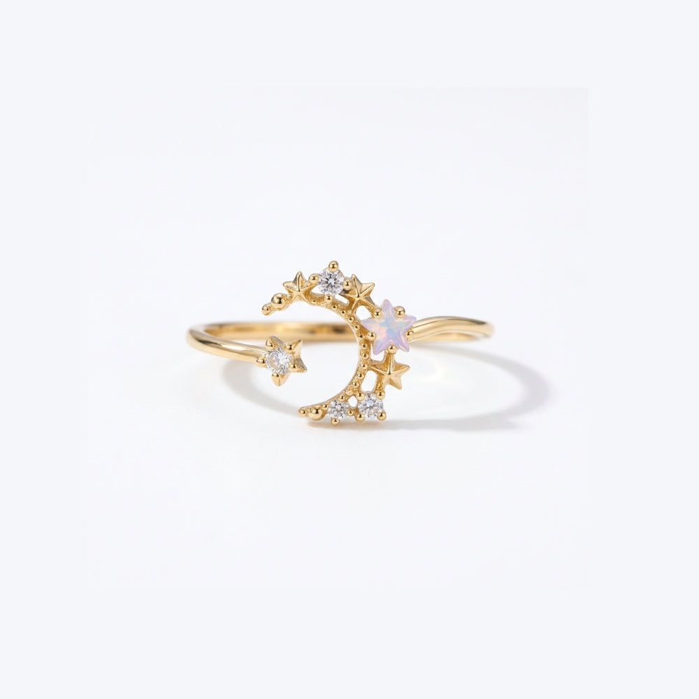A gold crescent moon and star ring with a small iridescent white opal-like center stone and clear accent stones, shown on a clean white background.