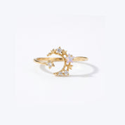 A gold crescent moon and star ring with a small iridescent white opal-like center stone and clear accent stones, shown on a clean white background.