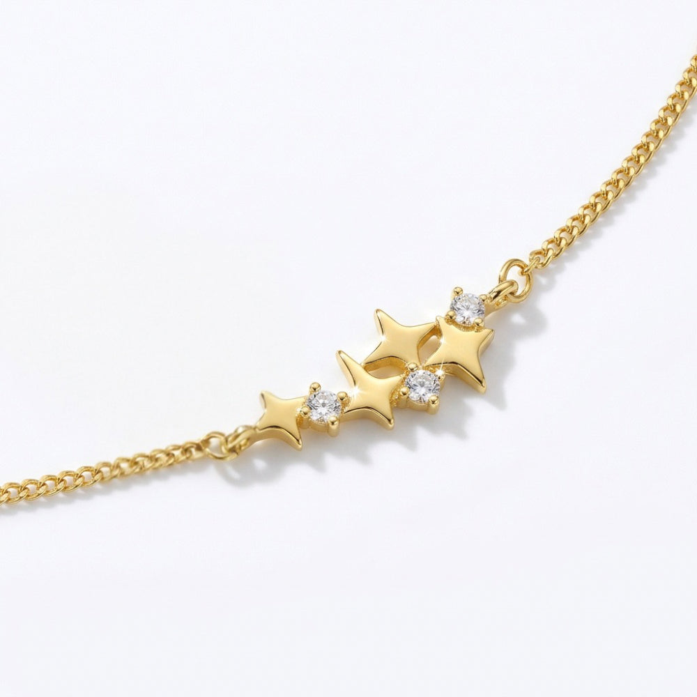 A gold chain bracelet featuring a central cluster of three gold stars, with the center star adorned with a small clear gemstone, set against a clean white background.
