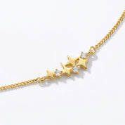 A gold chain bracelet featuring a central cluster of three gold stars, with the center star adorned with a small clear gemstone, set against a clean white background.