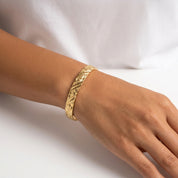 A close-up of a person's wrist wearing a textured gold bangle bracelet against a white background.