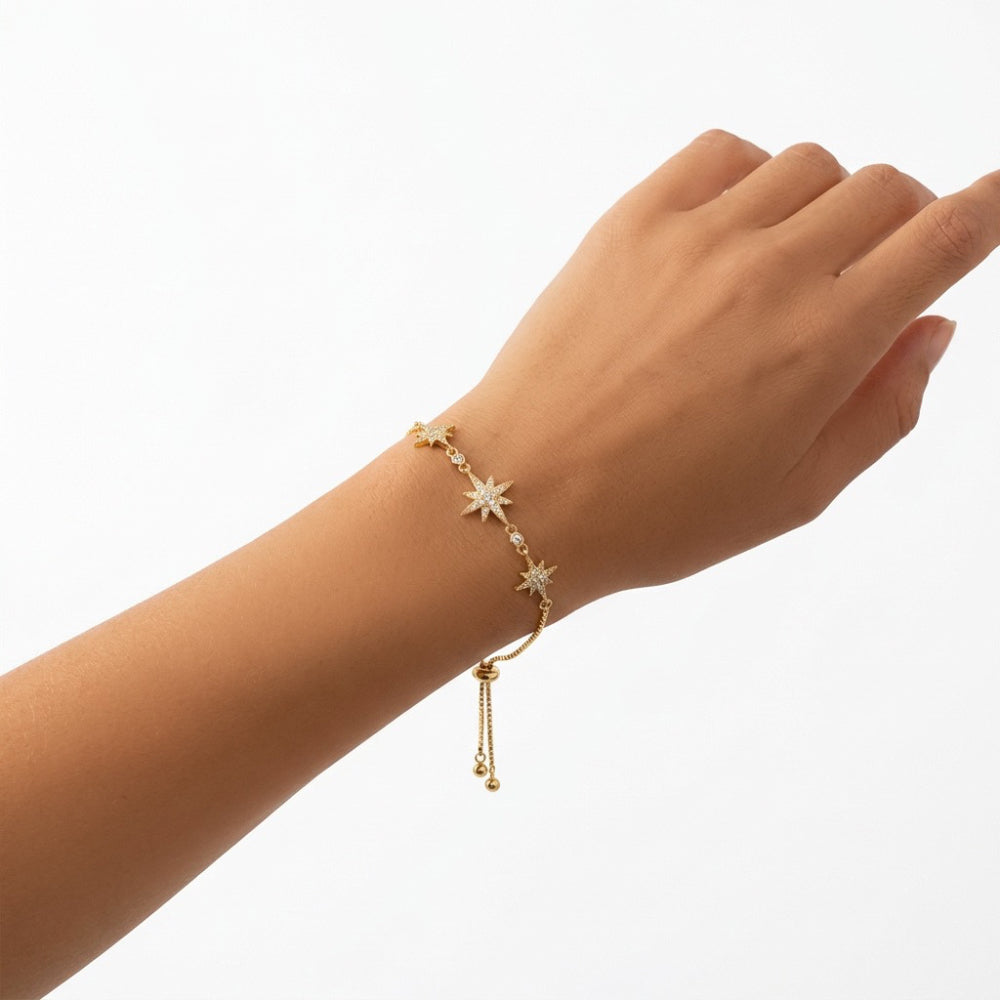 A delicate gold chain bracelet with star and bead details, shown worn on a person's wrist against a clean white background.
