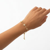 A delicate gold chain bracelet with star and bead details, shown worn on a person's wrist against a clean white background.