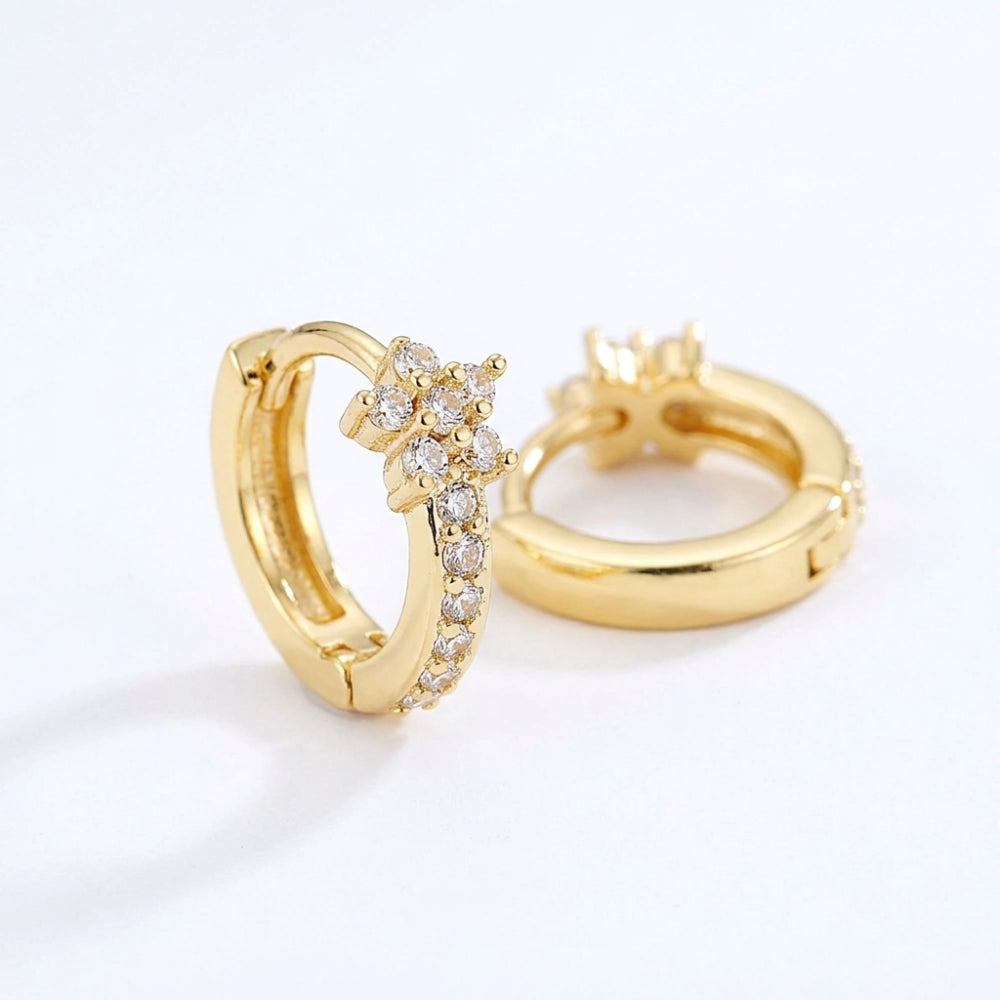A pair of gold huggie hoop earrings, one shown from the front with a floral cluster of clear stones and a pavé band, and the other from the side showing the clasp mechanism, on a white background.