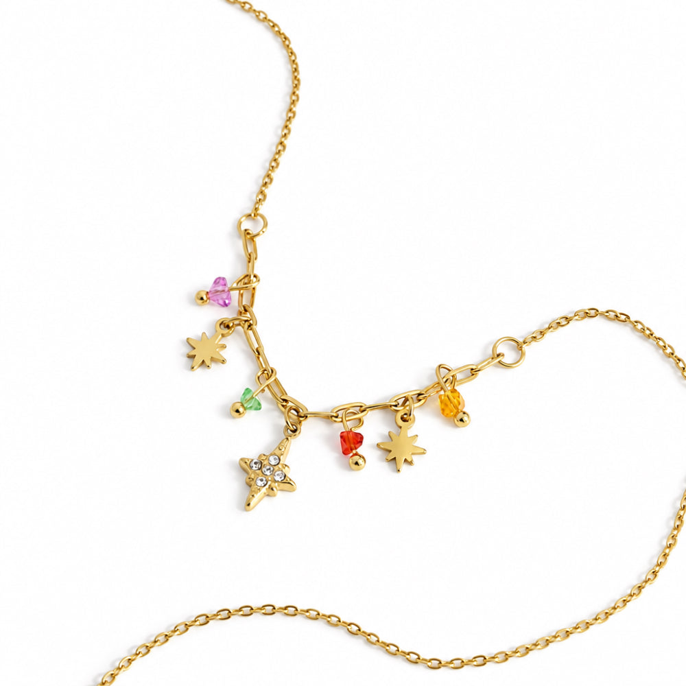 A gold-toned charm necklace featuring multiple small celestial and nature-themed pendants, including stars, a crescent moon, a flower, a bird, and colorful gem accents, displayed on a clean white background.