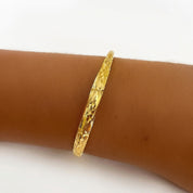 A textured yellow gold bangle bracelet worn on a person's wrist, shown against a plain white background.