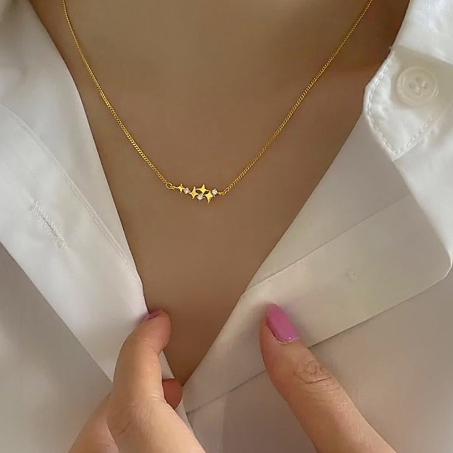  close-up of a person wearing a delicate gold necklace with a small geometric star-like pendant, styled with a white collared shirt.