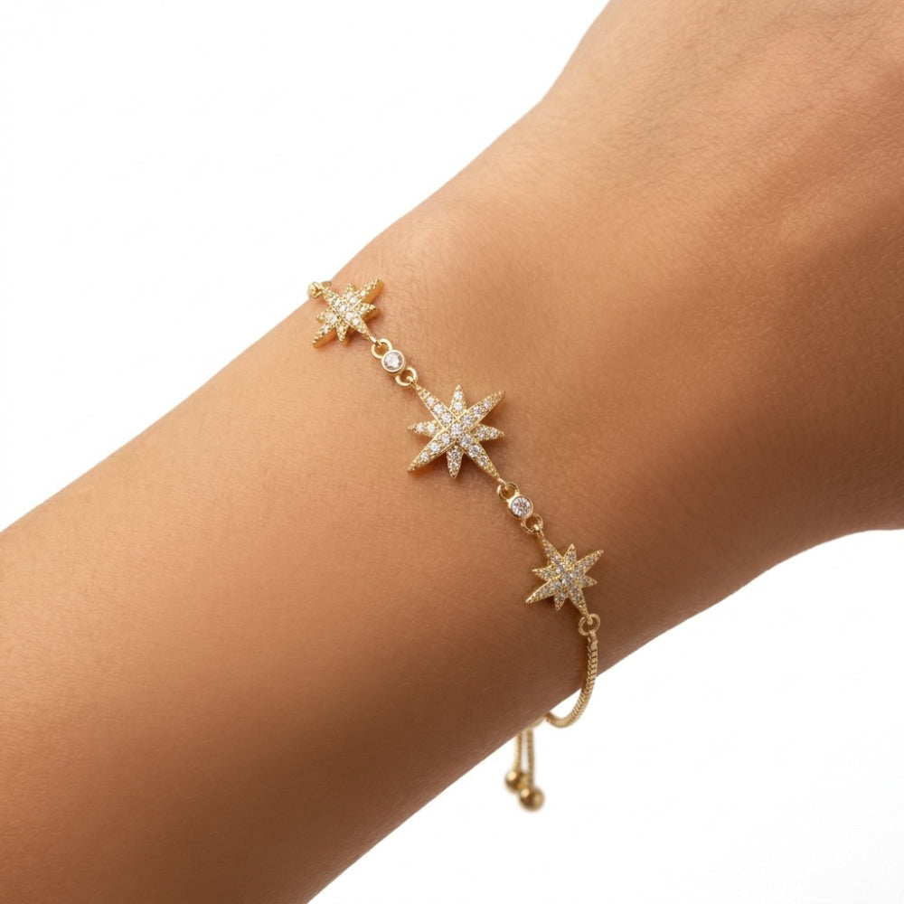 A delicate gold chain bracelet with three starburst charms set with small clear stones, shown worn on a person's wrist against a plain white background.
