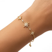 A delicate gold chain bracelet with three starburst charms set with small clear stones, shown worn on a person's wrist against a plain white background.