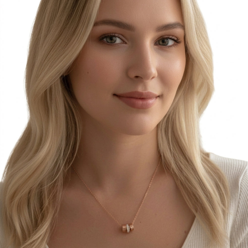 A close-up of a blonde woman wearing a delicate rose gold necklace with a small geometric pendant, set against a clean white background.