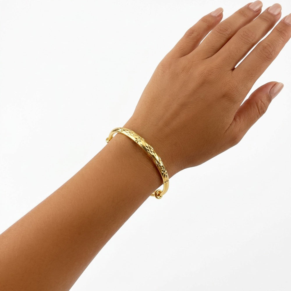 A gold textured bangle bracelet worn on a person's wrist, shown against a plain white background.