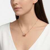 A close-up of a model wearing a delicate rose gold necklace with a cylindrical triple-band pendant, styled with a white V-neck top against a clean white background.