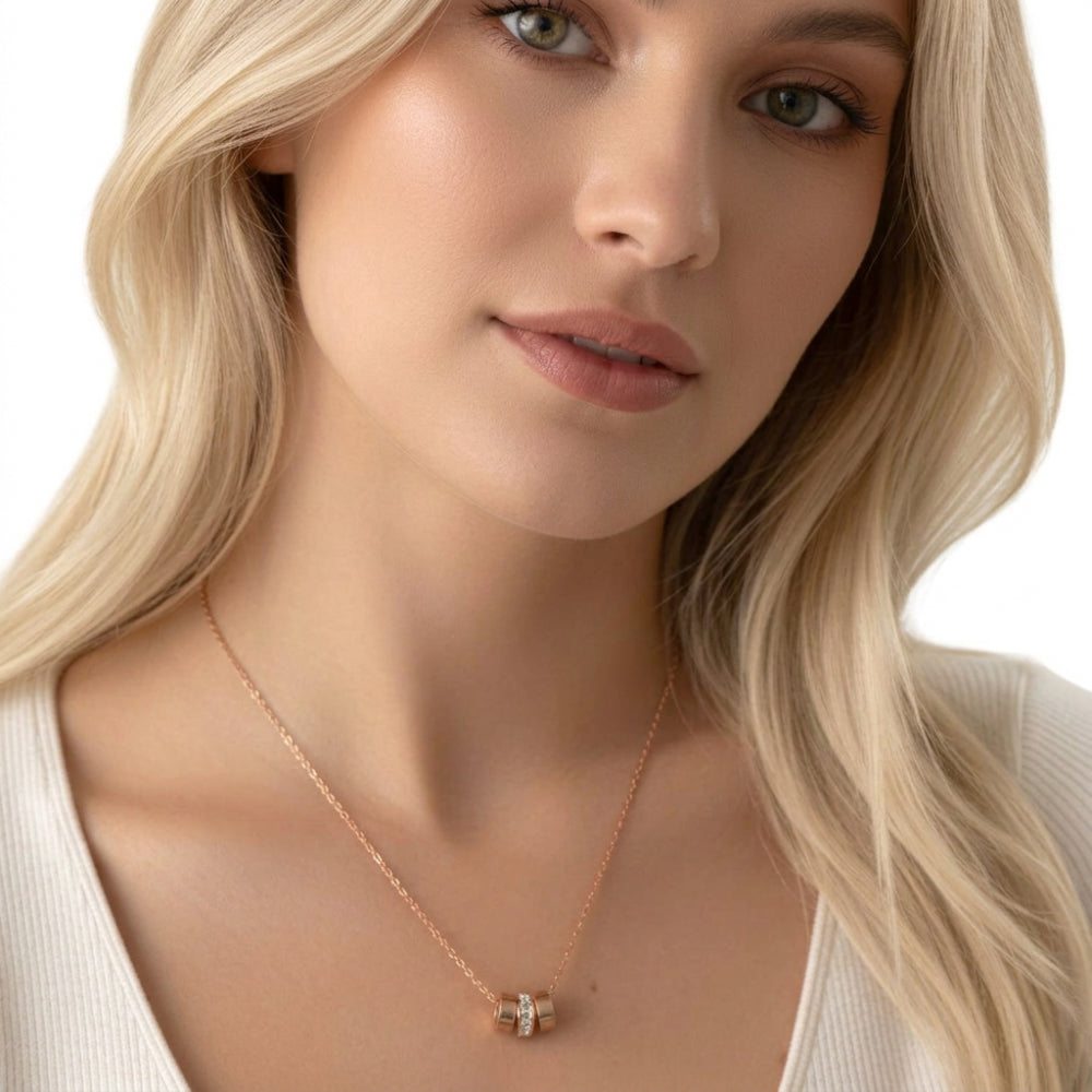 A close-up of a blonde woman wearing a delicate rose gold necklace with a small geometric pendant, set against a clean white background.
