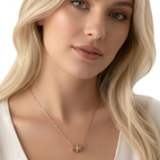 A close-up of a blonde woman wearing a delicate rose gold necklace with a small geometric pendant, set against a clean white background.
