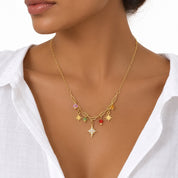A gold necklace with a central star charm and small colorful star and bead charms, shown worn on a model's neck over a white collared shirt.