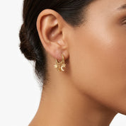 Model wearing a dainty gold huggie earrings with dangling star and crescent moon charms 
