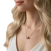 A close-up lifestyle shot of a woman wearing a delicate rose gold necklace with a small cylindrical bead pendant, styled with a white top against a clean white background.