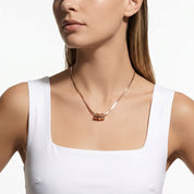 A close-up of a woman wearing a delicate rose gold chain necklace with a small bow-shaped pendant, paired with a white tank top against a clean white background.