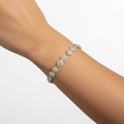 A close-up of a delicate gold tennis bracelet with round floral clusters of clear stones, shown worn on a person's wrist against a clean white background.
