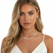 A blonde woman with blue eyes wearing a delicate silver-toned necklace with sparkling clear stones and a matching stud earring, photographed against a clean white background
