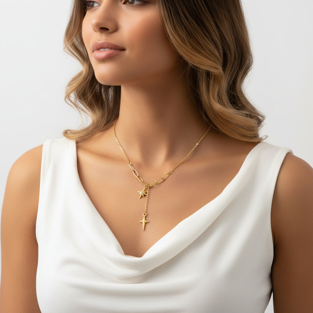A woman wearing a delicate gold necklace with a Y-shaped design featuring a star and cross pendant, styled with a white sleeveless top against a light gray background.