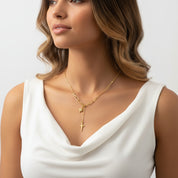 A woman wearing a delicate gold necklace with a Y-shaped design featuring a star and cross pendant, styled with a white sleeveless top against a light gray background.