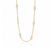 A delicate gold chain necklace featuring seven small pear-cut clear gemstones spaced along the chain, displayed on a clean white background with a soft reflection below.