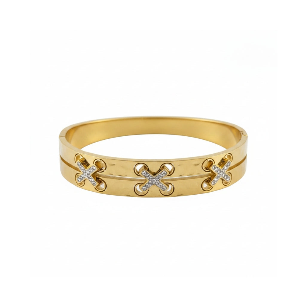A gold bangle bracelet featuring three interlocking 'X' motifs, with two of the 'X's embellished with small clear pavé stones, set against a plain white background.