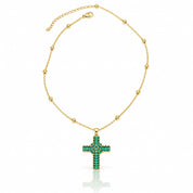 A gold chain necklace with a cross pendant adorned with green gemstones, displayed on a clean white background with a soft reflection below.