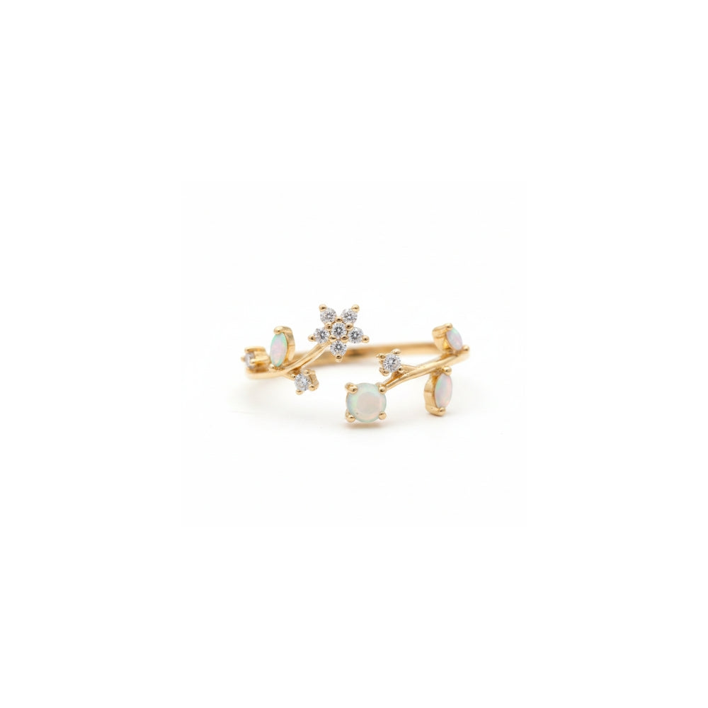 A delicate gold ring featuring a floral branch design with white opal-like round stones and small clear crystal accents, photographed on a seamless white background.