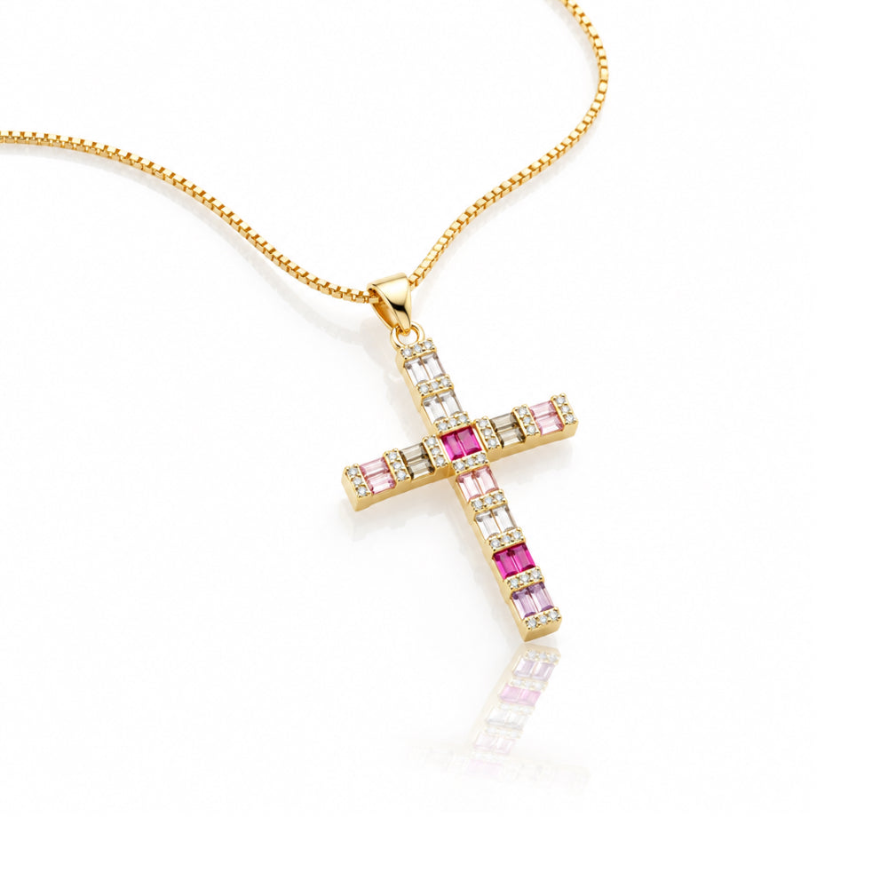 A gold cross pendant necklace adorned with pink and clear rectangular gemstones, suspended from a gold chain on a white background with a soft reflection.