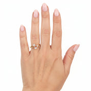 A close-up of a hand with pale pink manicured nails wearing a delicate gold ring with small clear stones, set against a plain white background.