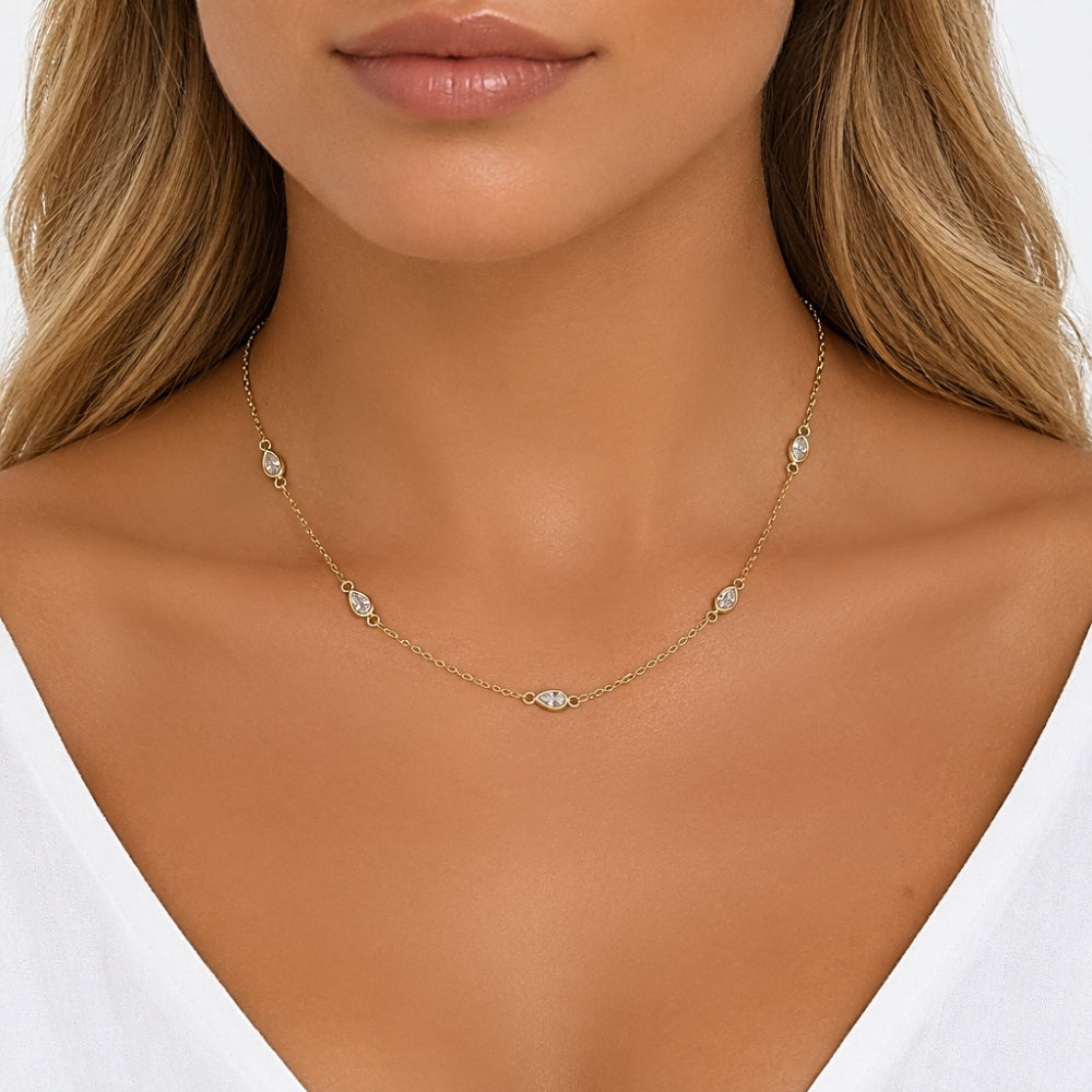 A close-up of a model wearing a delicate gold chain necklace with small, clear oval gemstones spaced along the chain.