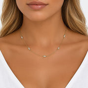 A close-up of a model wearing a delicate gold chain necklace with small, clear oval gemstones spaced along the chain.