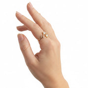A delicate gold ring with small clear gemstones worn on a person's ring finger, shown against a plain white background.