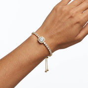 A close-up of a person's wrist wearing a delicate bracelet with a round pavé center stone and gold-toned chain drop charms, shown against a plain white background.