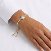 A gold-plated adjustable bracelet with a round pavé center stone and a row of small clear stones, shown worn on a person's wrist against a white background.