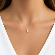 A close-up of a model's neck and chest wearing a delicate silver chain necklace with a small marquise-cut clear gemstone pendant.