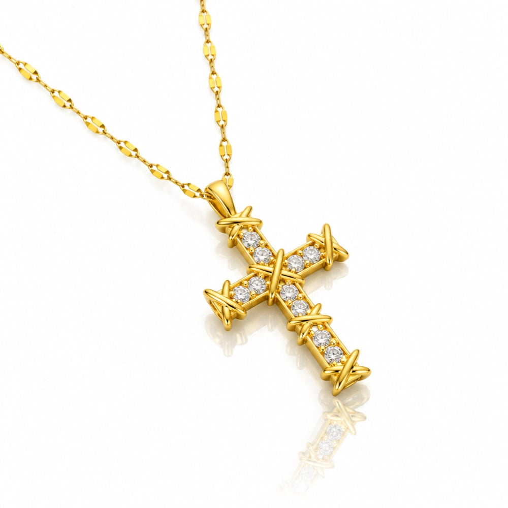 A gold cross pendant necklace adorned with small clear stones along its edges, suspended from a gold link chain on a clean white background with a soft reflection.