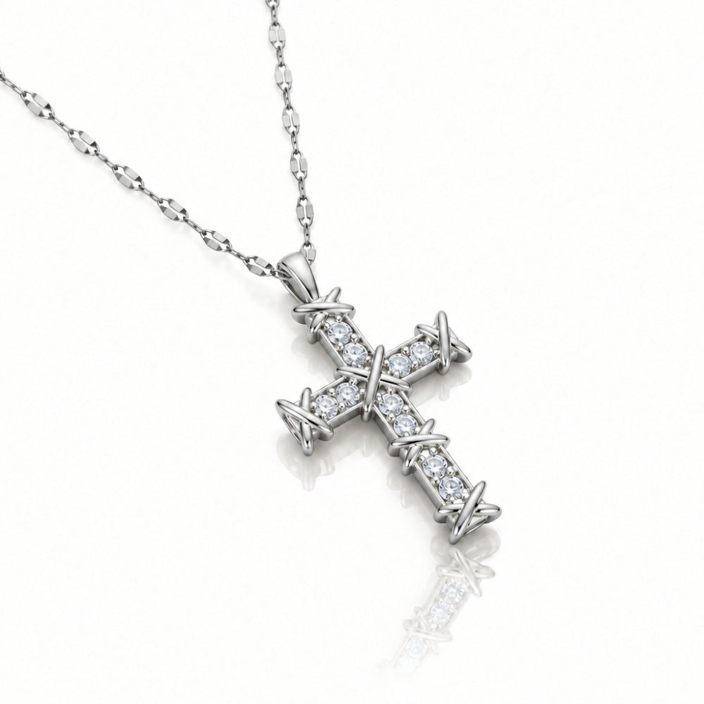 A silver cross pendant necklace paved with small clear stones, featuring a barbed wire design at the ends, shown on a white background with a soft reflection.
