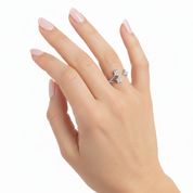 A close-up of a hand with pale pink manicured nails wearing a silver ring with three small clear gemstones, set against a plain white background.