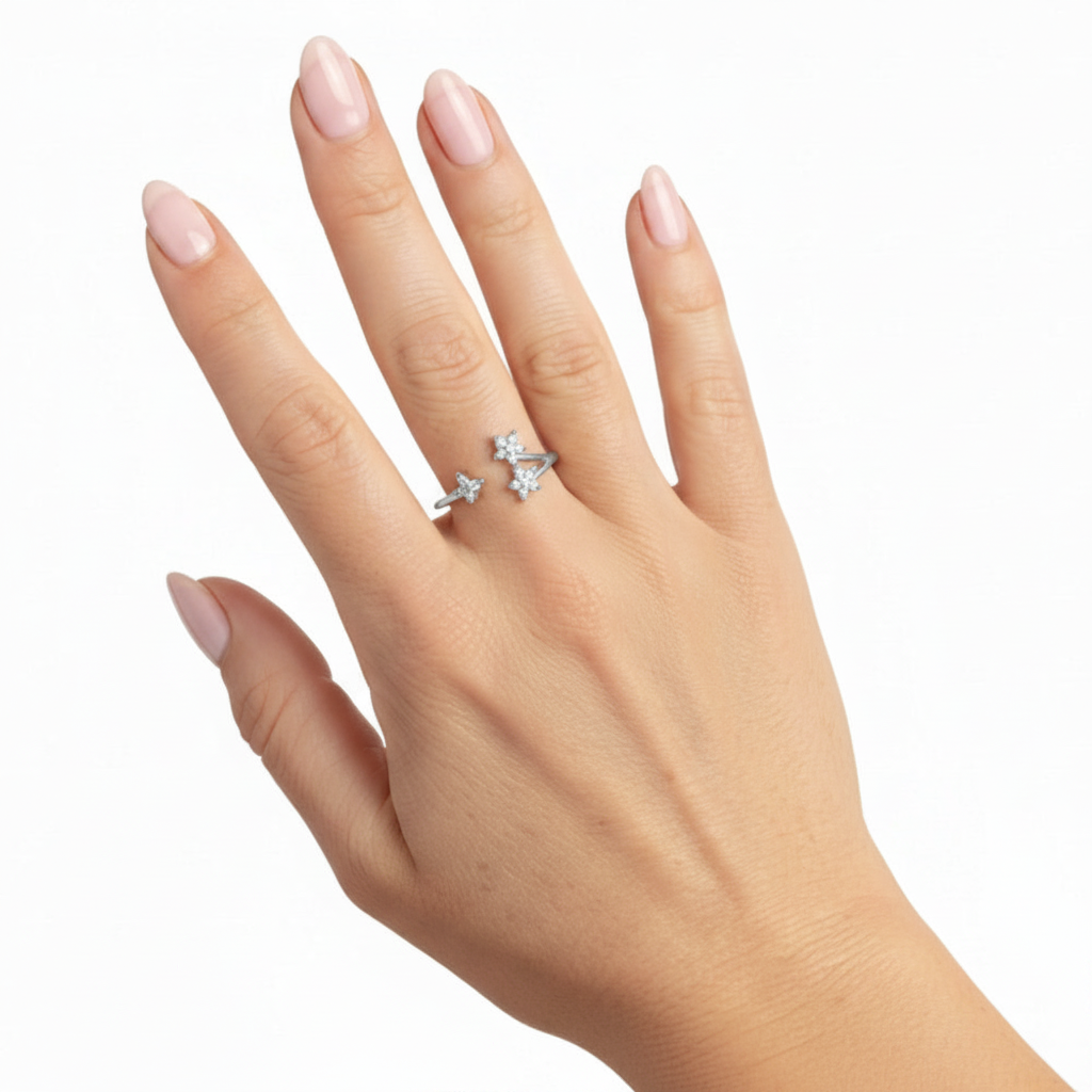A close-up of a hand with pale pink manicured nails wearing a silver-toned ring with three small clear gemstones in a row, set against a plain white background.