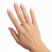 A close-up of a hand with pale pink manicured nails wearing a silver-toned ring with three small clear gemstones in a row, set against a plain white background.