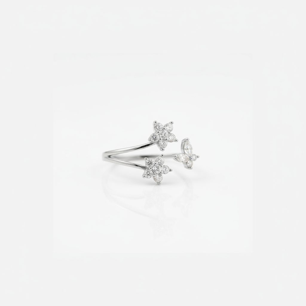 A delicate silver ring featuring three small star and flower and butterfly motifs set with clear stones, displayed on a clean white background with a soft reflection.